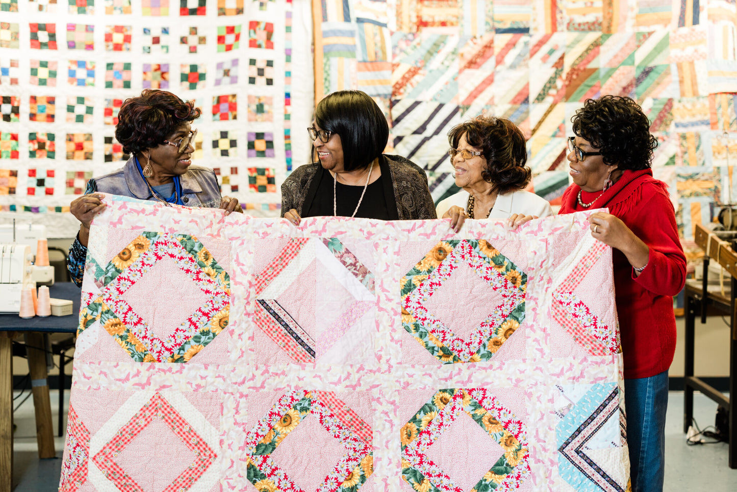 four ladies holding a pink quilt