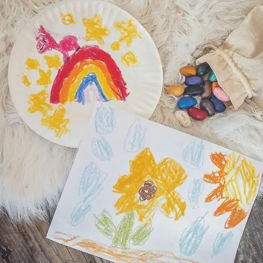 Children's drawings of a rainbow and flowers on paper plates, with crayons on a fluffy surface.