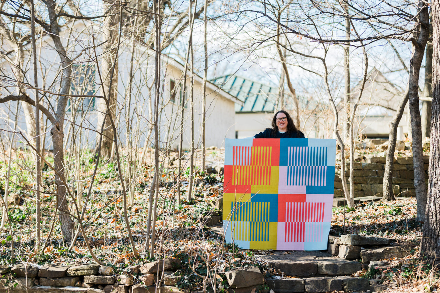 a woman holding a striped quilt in the woods