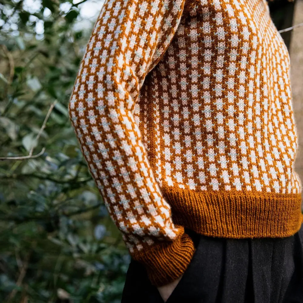 Knitted sweater with a brown and white pattern worn by a person, blurred green background