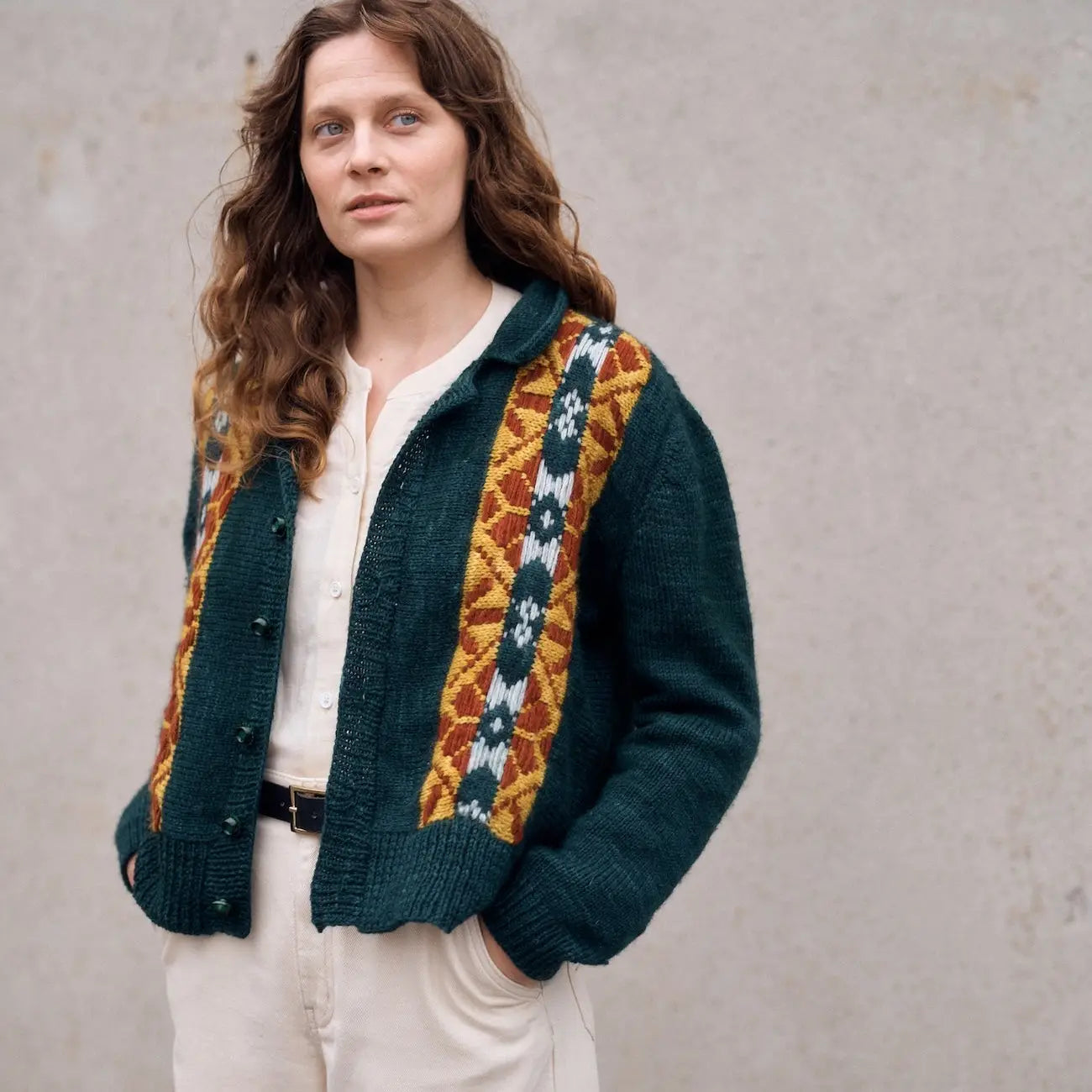 Woman wearing a green knitted cardigan with colorful pattern against a plain background