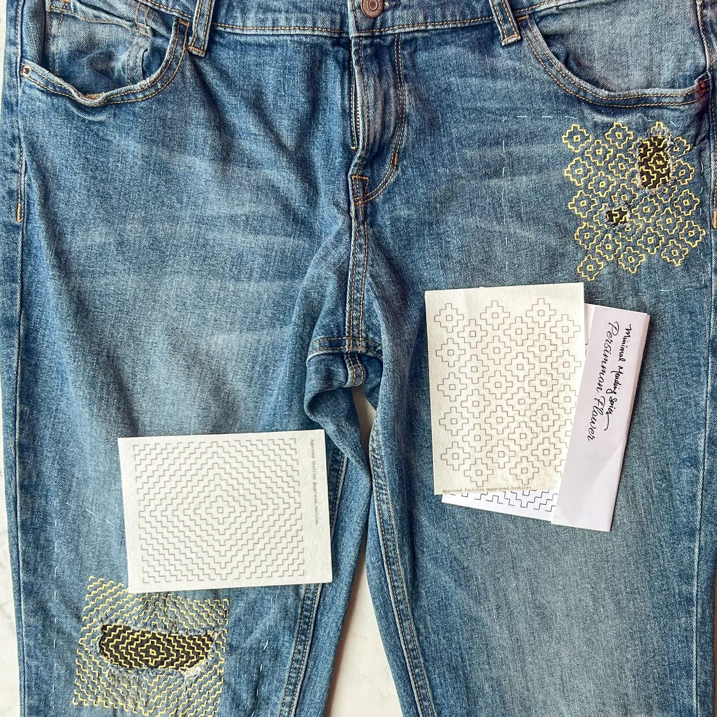 Blue jeans with decorative patches and patterns on a white background