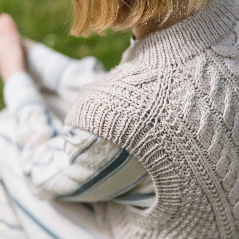 Person wearing a cable knit sweater sitting outdoors