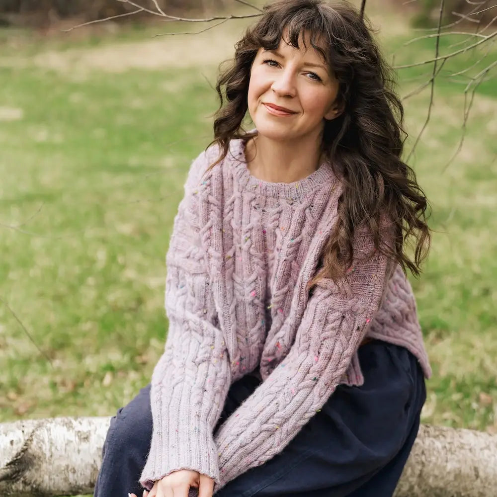 Woman wearing a pink knitted sweater sitting on a log in a park.