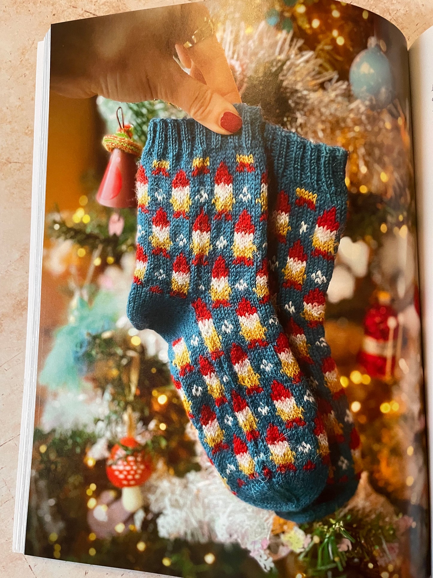 Colorful knitted gnome socks held by a hand against a festive background with lights and decorations.
