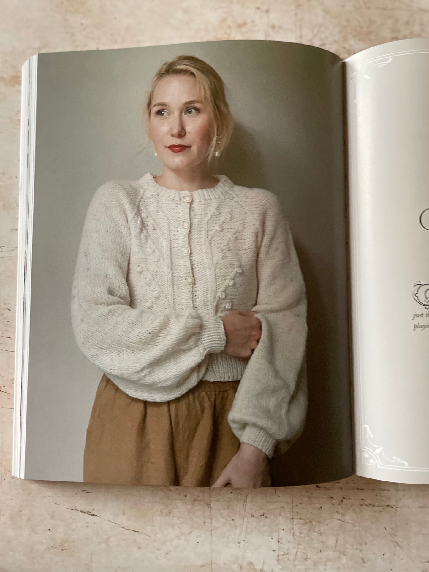 Open book showing a woman wearing a cream sweater with cables and bobbles and brown skirt.