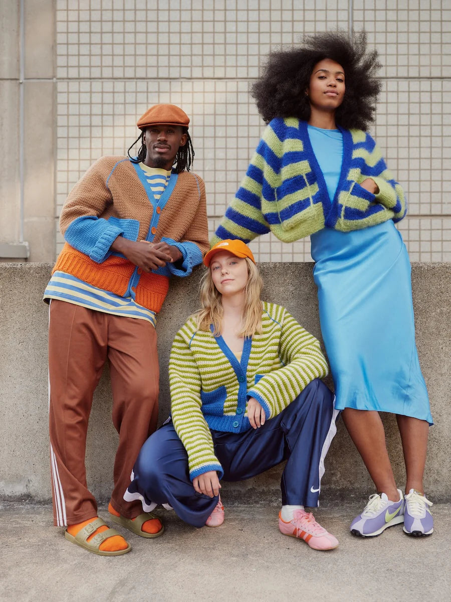 Three people wearing colorful knitted cardigans against a tiled wall.