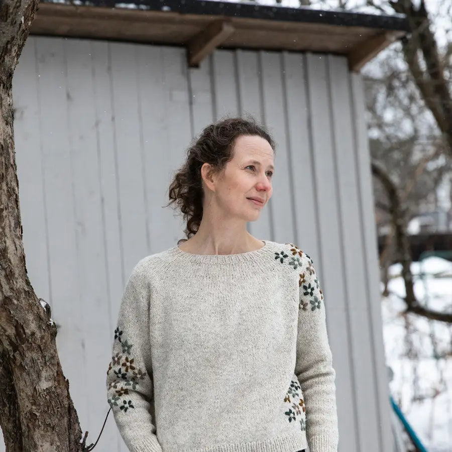 a woman wearing a cream sweater with embroidered knit flowers
