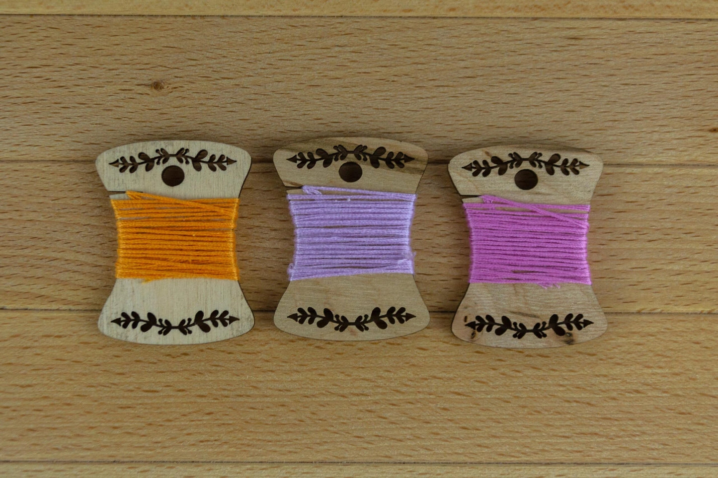 3 engraved wooden bobbins wrapped in thread