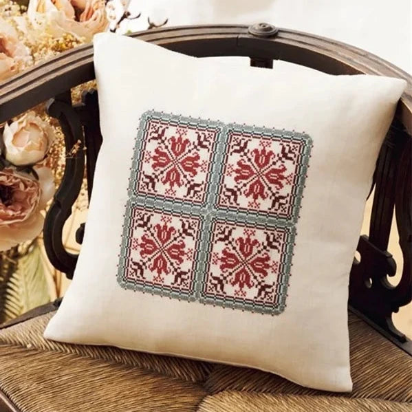a red and green cross stitch design on a white pillow
