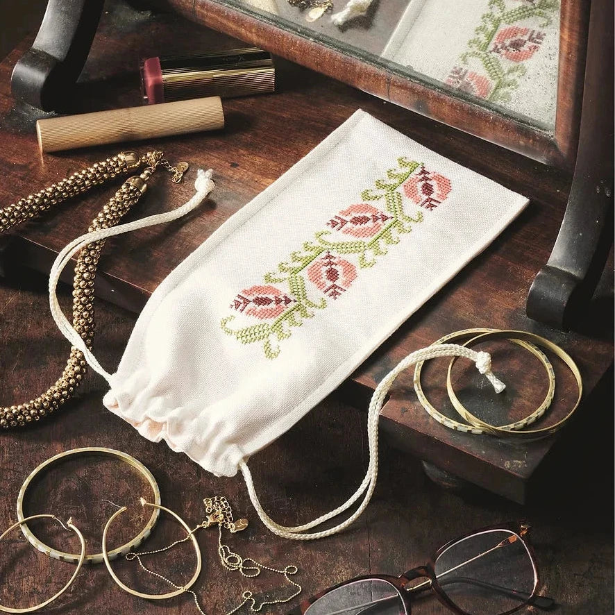 Cross stitch embroidery kit supplies on a vanilla linen fabric surface, including DMC floss, tapestry needle, and other embroidery tools.