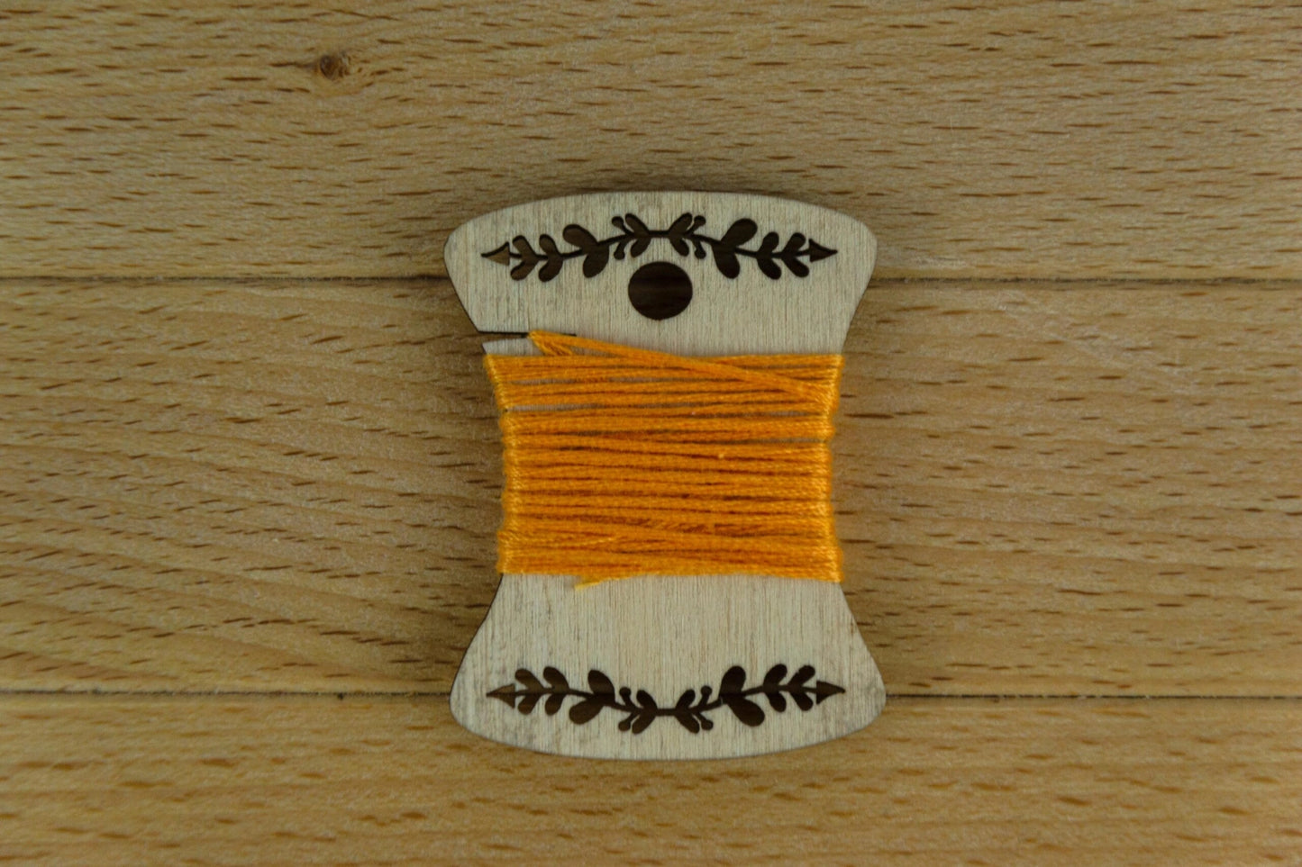 an engraved wooden bobbin wrapped in orange embroidery thread