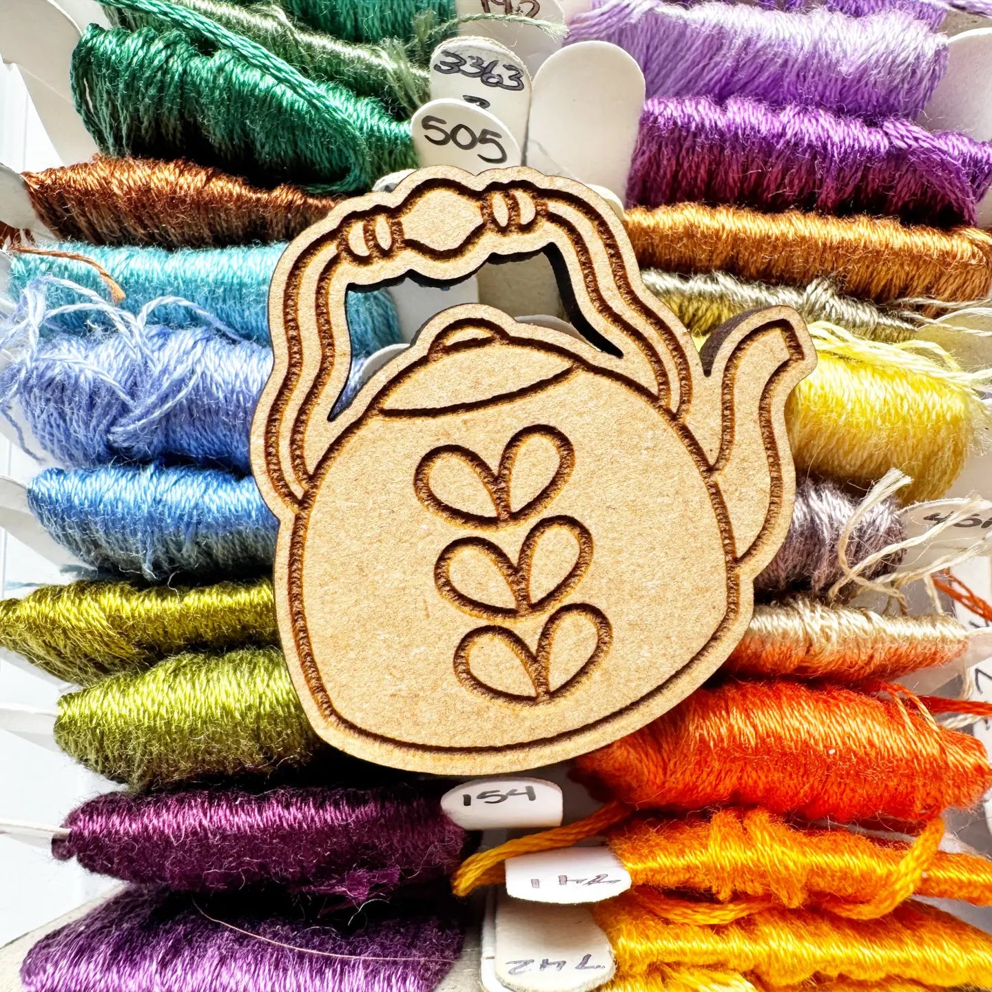 Wooden needle minder with floral design on a background of colorful embroidery threads.