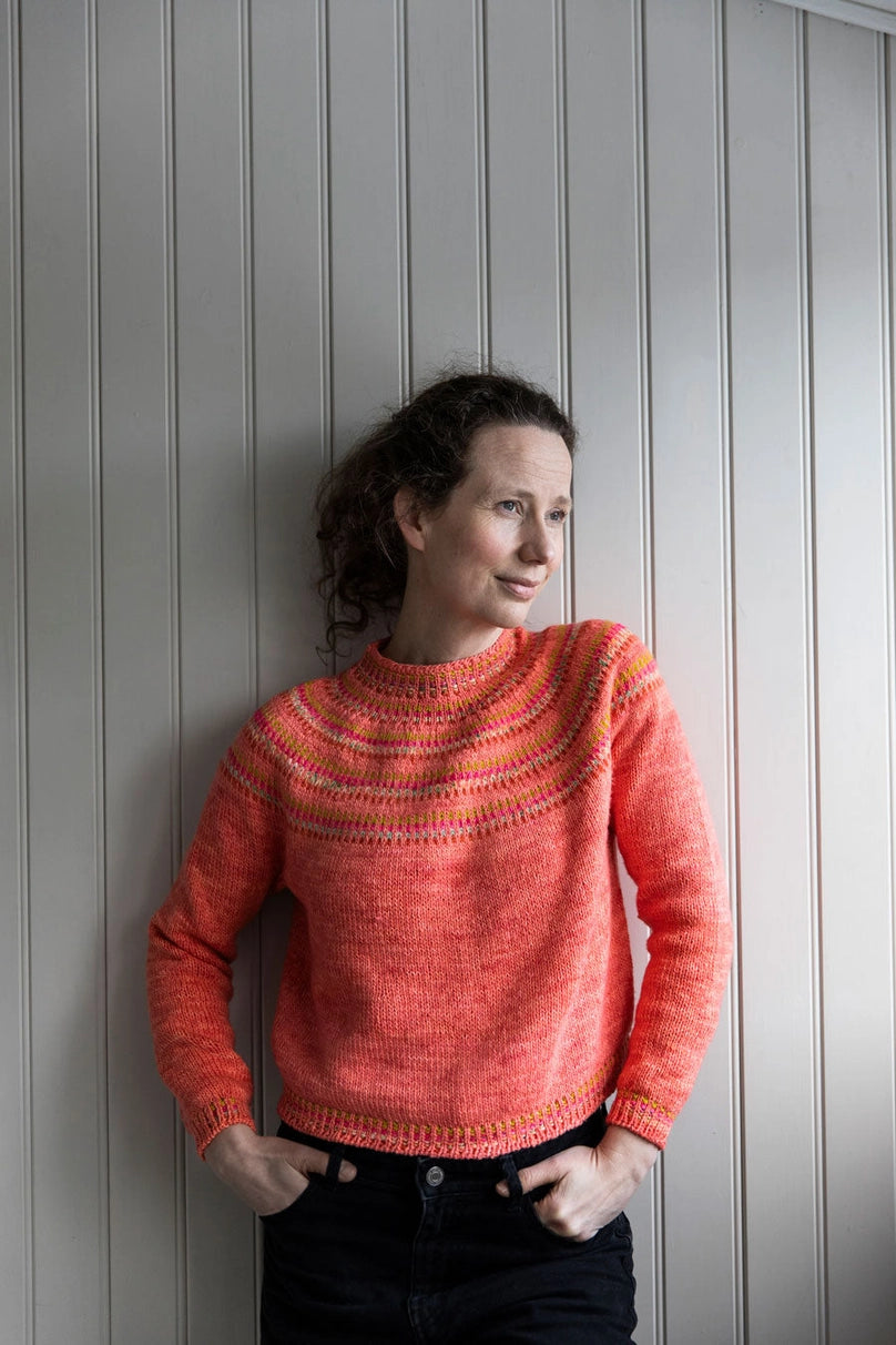a woman wearing a coral pink sweater with a colorful yoke