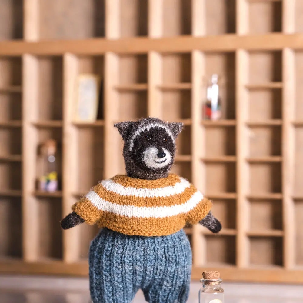 a knitted raccoon wearer a yellow striped sweater