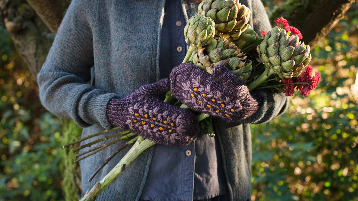 a person with purple embroidered mittens holding flowers
