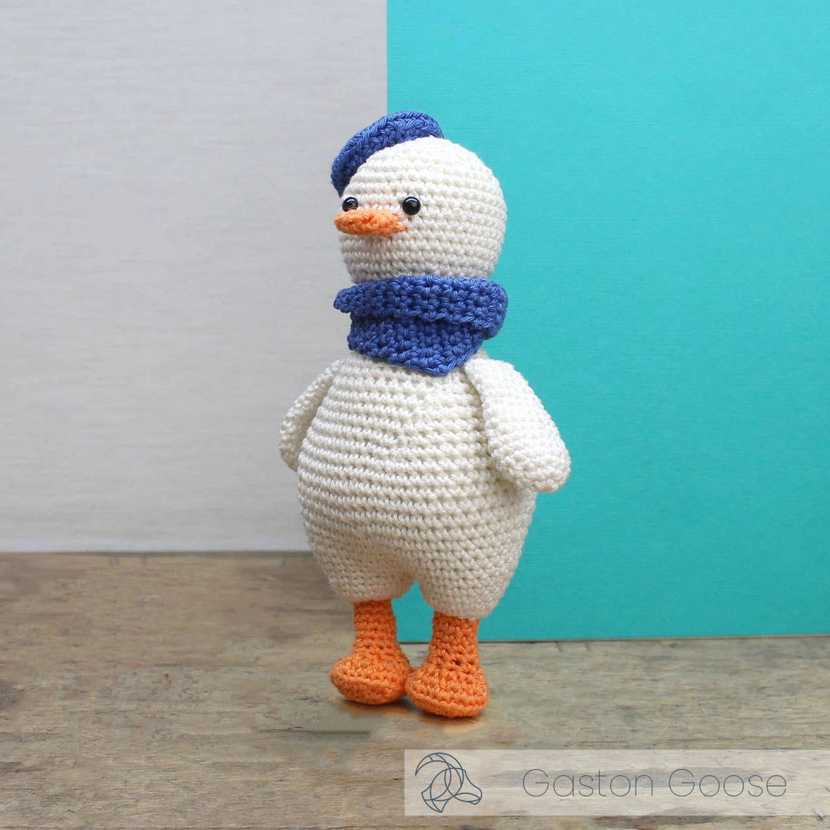 Crocheted goose toy with a blue hat and scarf against a teal and gray background