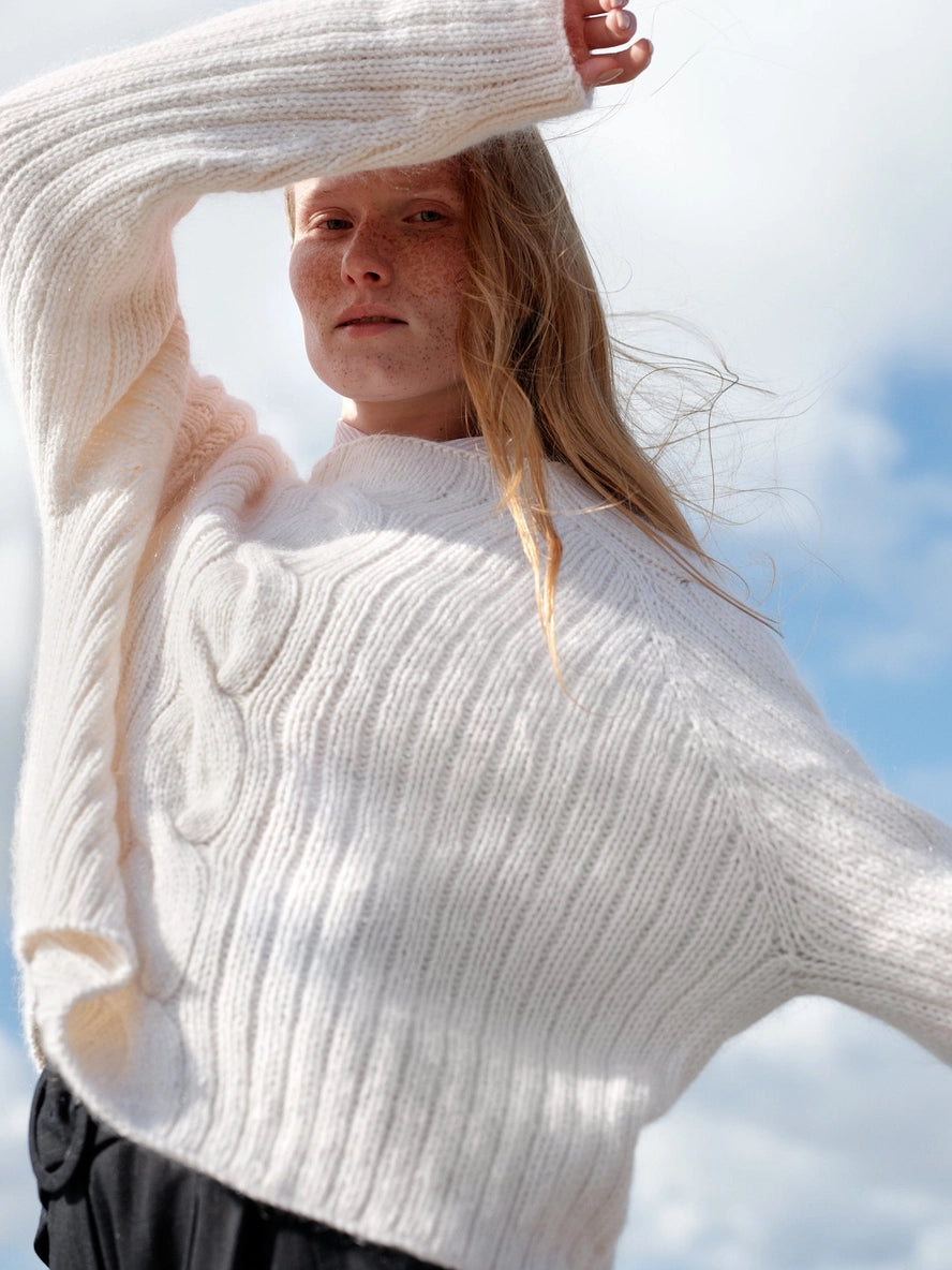 Woman wearing a white knitted sweater with a blurred background