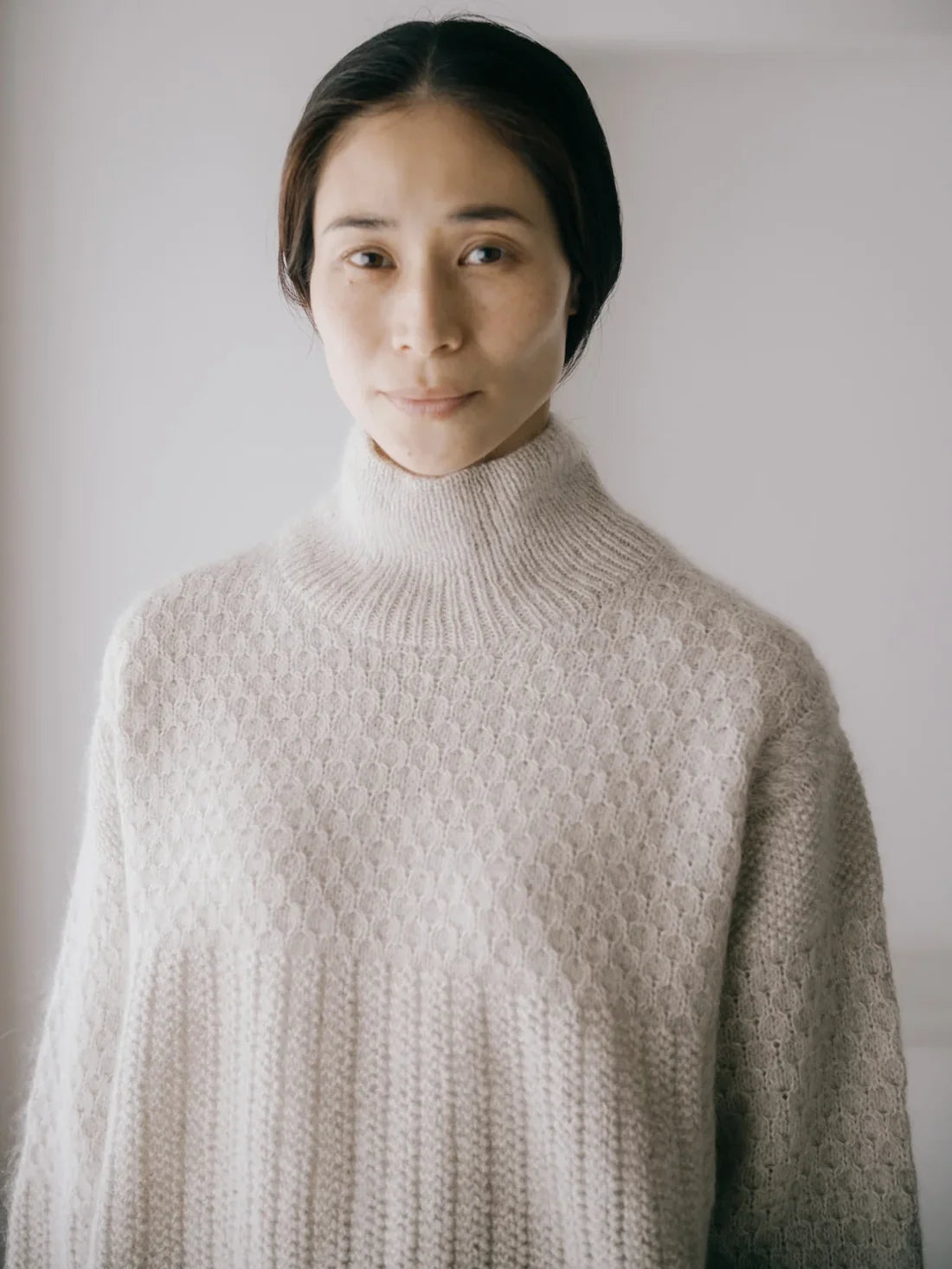 a woman wearing a turtleneck textured hand knit sweater in a neutral color