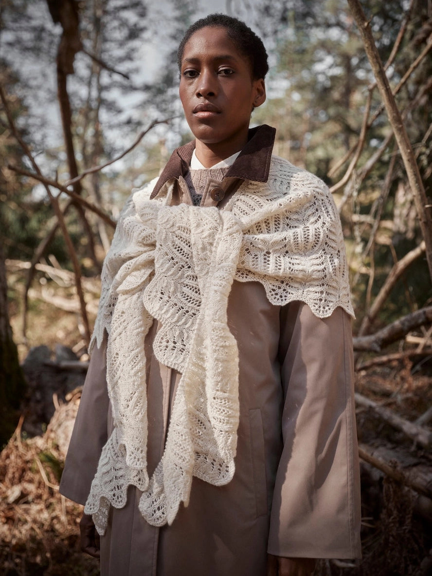 Person wearing a beige coat and white lace shawl in a forest setting