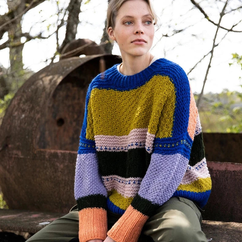 Person wearing a colorful striped sweater sitting outdoors.