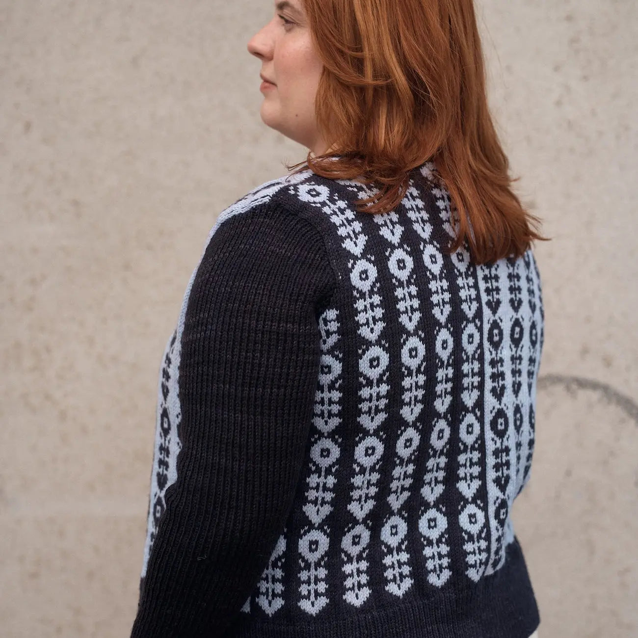 Person wearing a black and white patterned sweater against a plain background