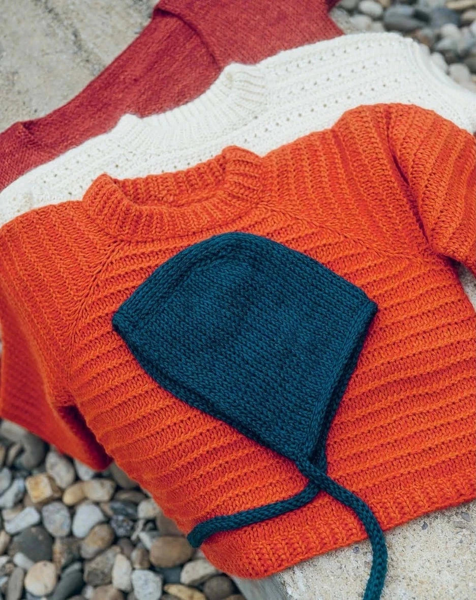 Knitted orange sweater with blue hat on pebbles
