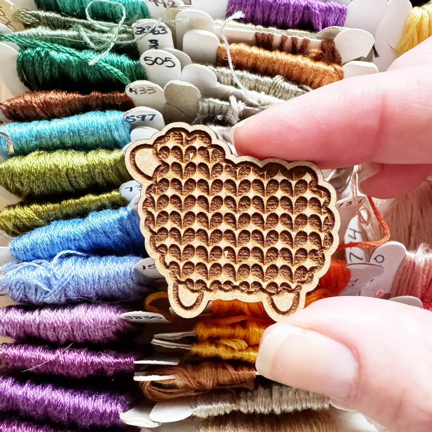 Wooden sheep-shaped needle minder held over spools of colorful thread.