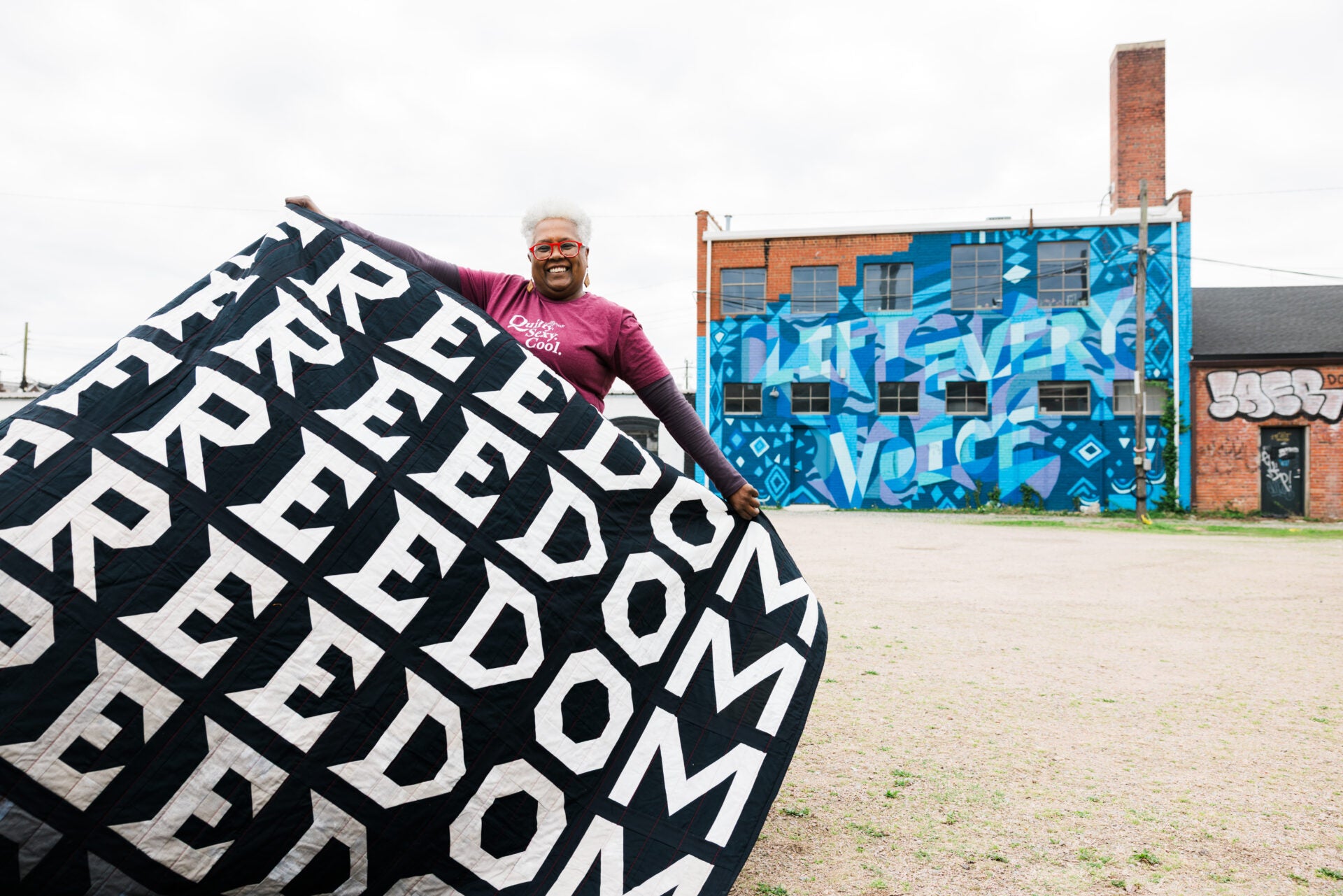 Person holding a large 'Freedom' flag with a graffiti-covered building in the background