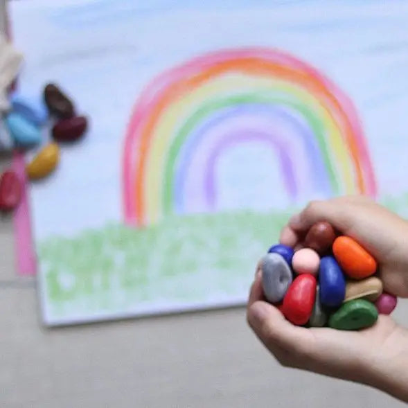 Colorful crayon stones held by a hand with a drawing of a rainbow in the background