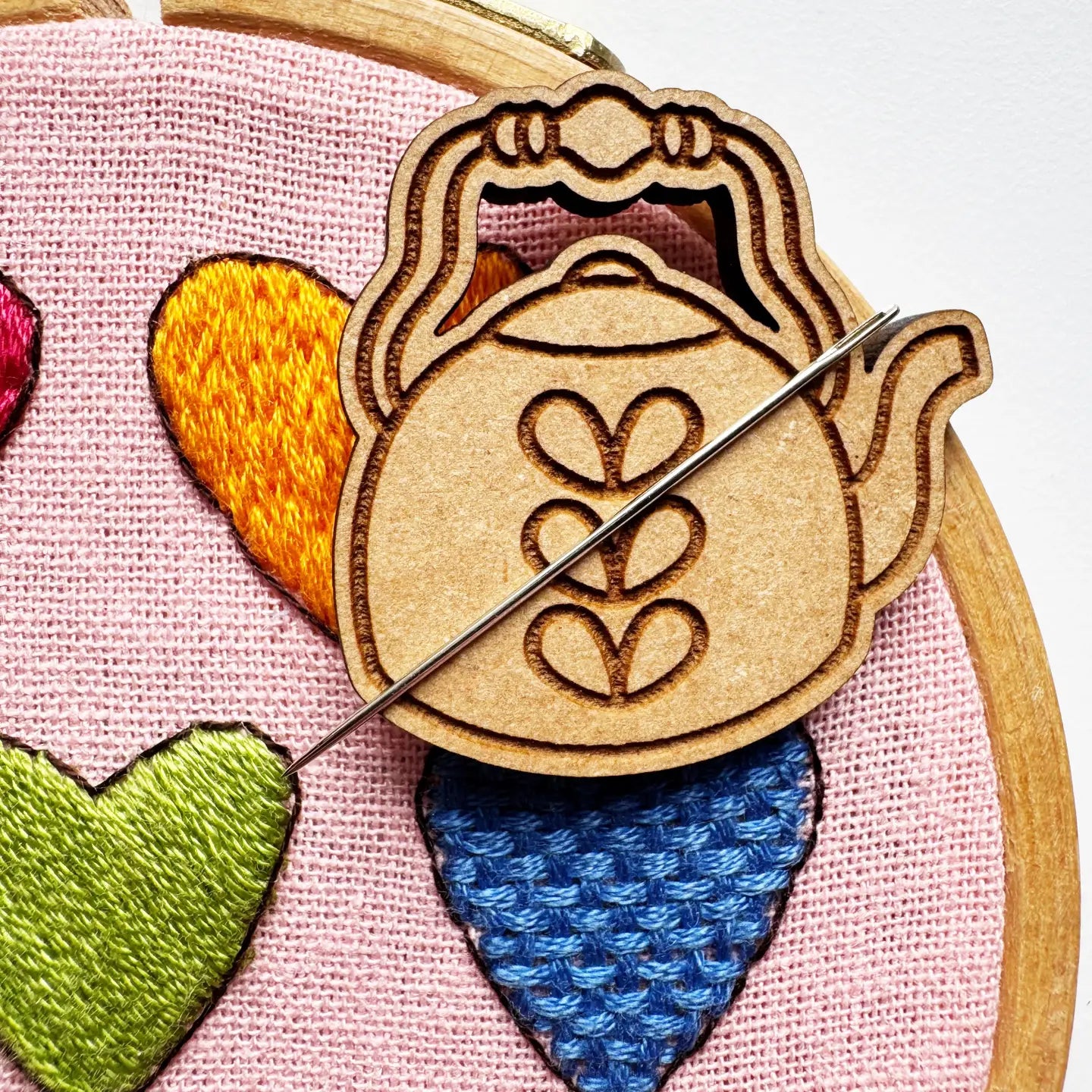Embroidery hoop with colorful fabric hearts and a wooden teapot-shaped needle minder