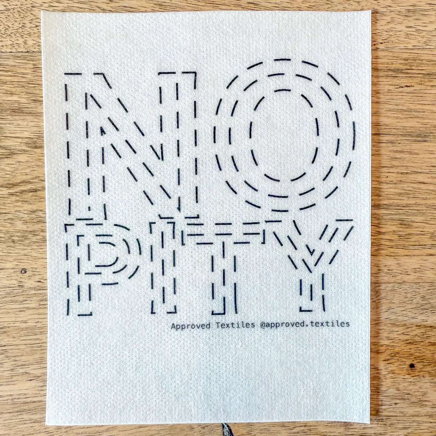 Dissolvable stitching guide with No Pity  on a wooden surface, featuring the brand 'approved.textiles'.