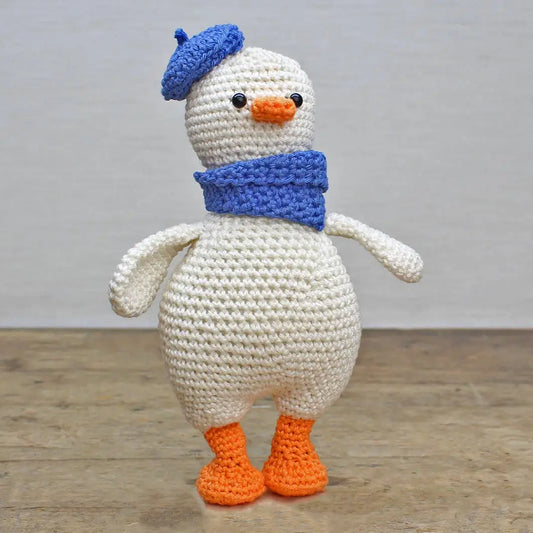 Crocheted goose toy with a blue hat and scarf on a wooden floor.