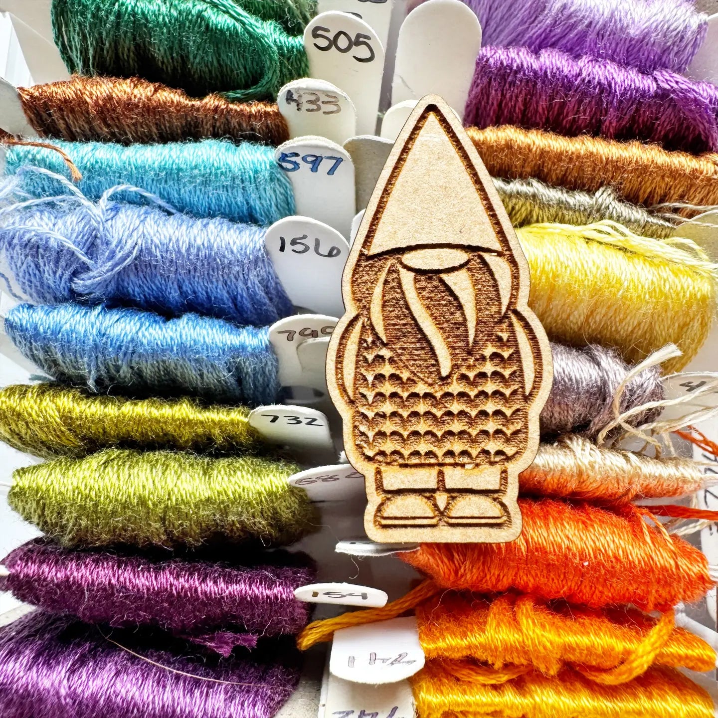 Wooden gnome needle minder with colorful thread spools in the background