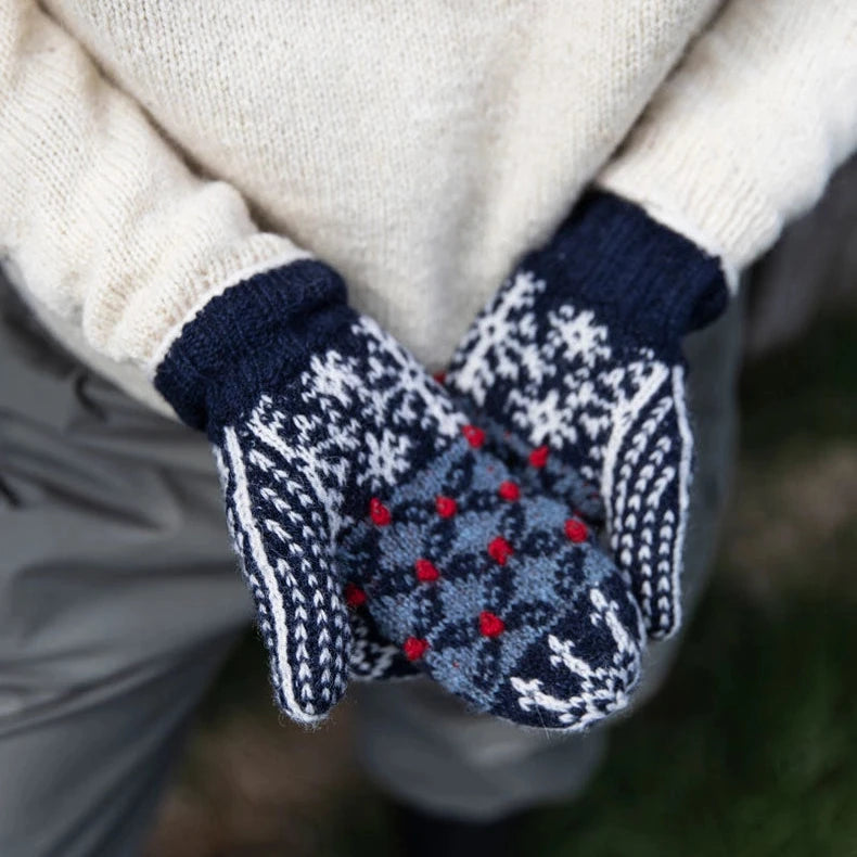 Close-up of a person wearing navy and white patterned mittens with red accents.