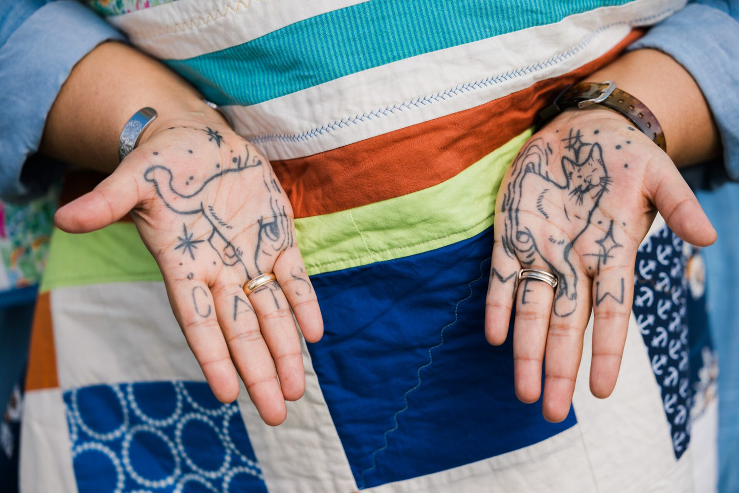 Close-up of hands with tattoos against a colorful quilted fabric background