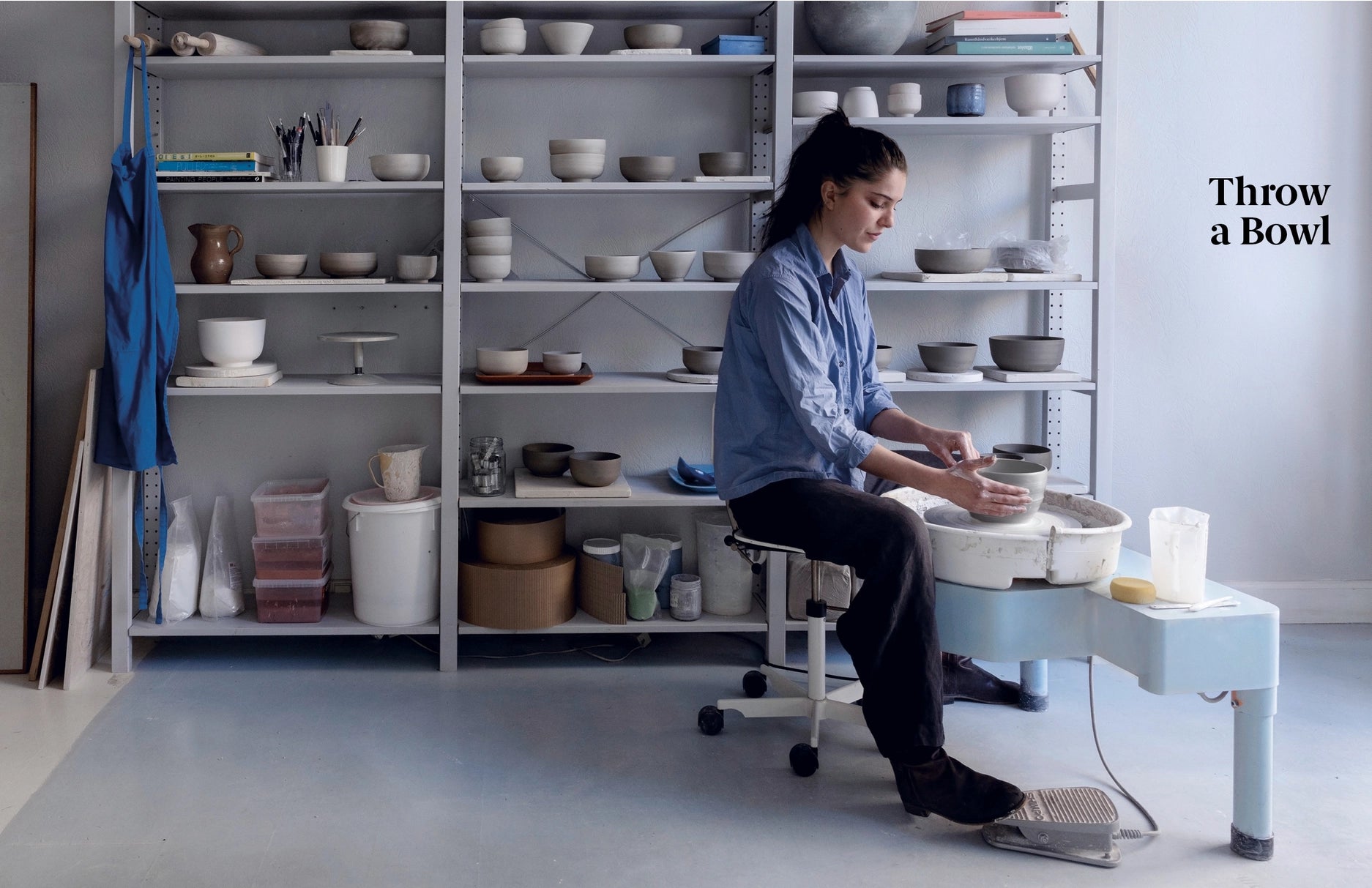 Person working on a pottery wheel in a studio with shelves of ceramic items.