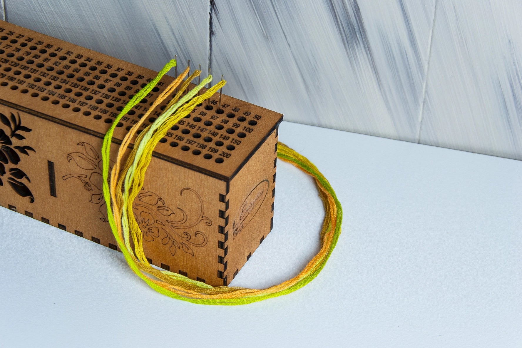 Wooden box with decorative patterns and yellow threaded needles on a light background