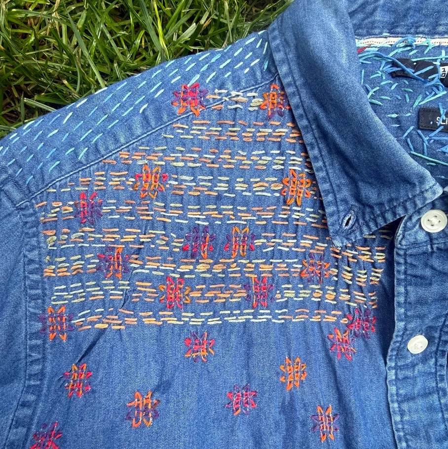 Blue denim shirt with intricate embroidery on a grassy background