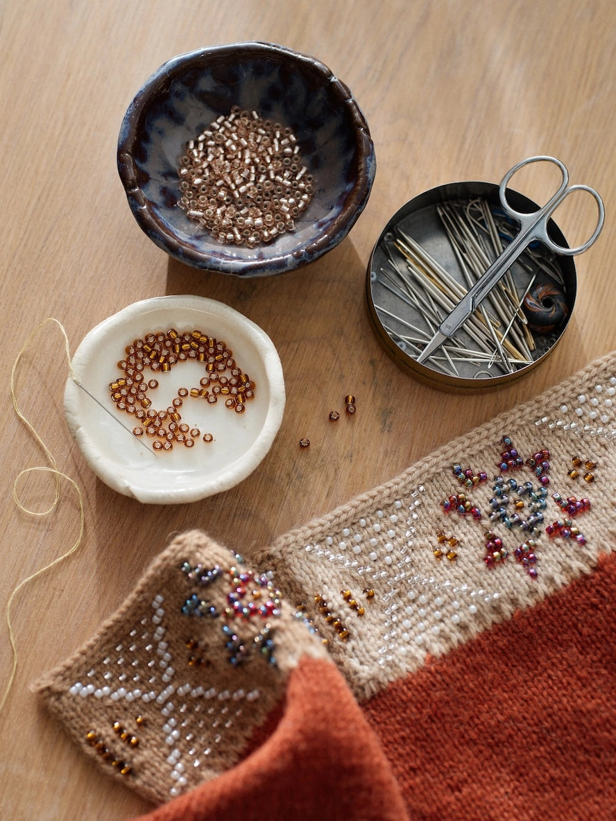 Crafting materials including beads, scissors, and a partially completed beaded project on a wooden surface.