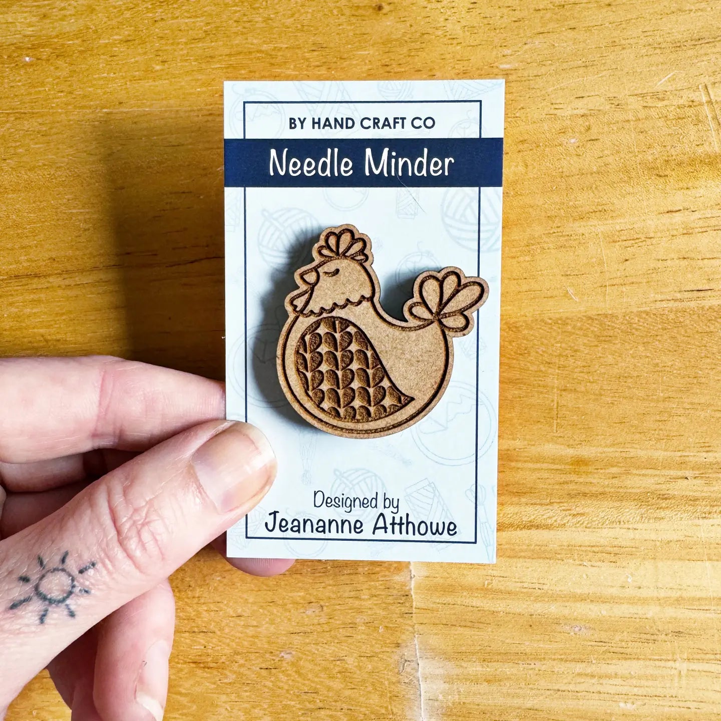 Wooden needle minder with packaging labeled 'By Hand Craft Co' on a wooden surface.