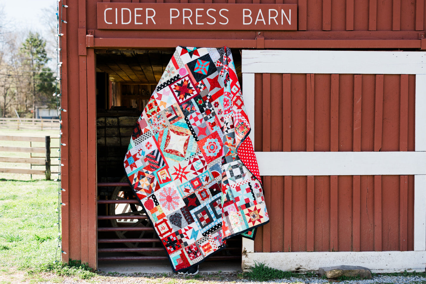 Colorful quilt draped over a wooden door of a building labeled 'Cider Press Barn'.