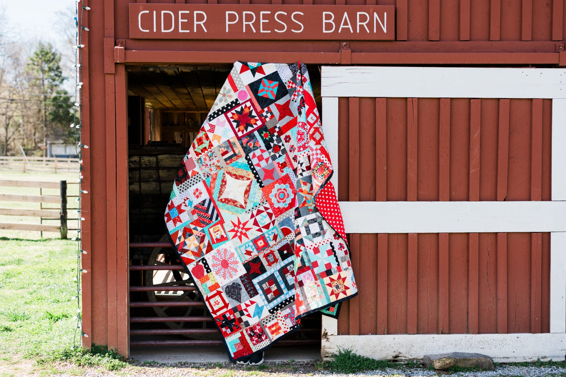 Colorful quilt draped over a wooden door of a building labeled 'Cider Press Barn'.