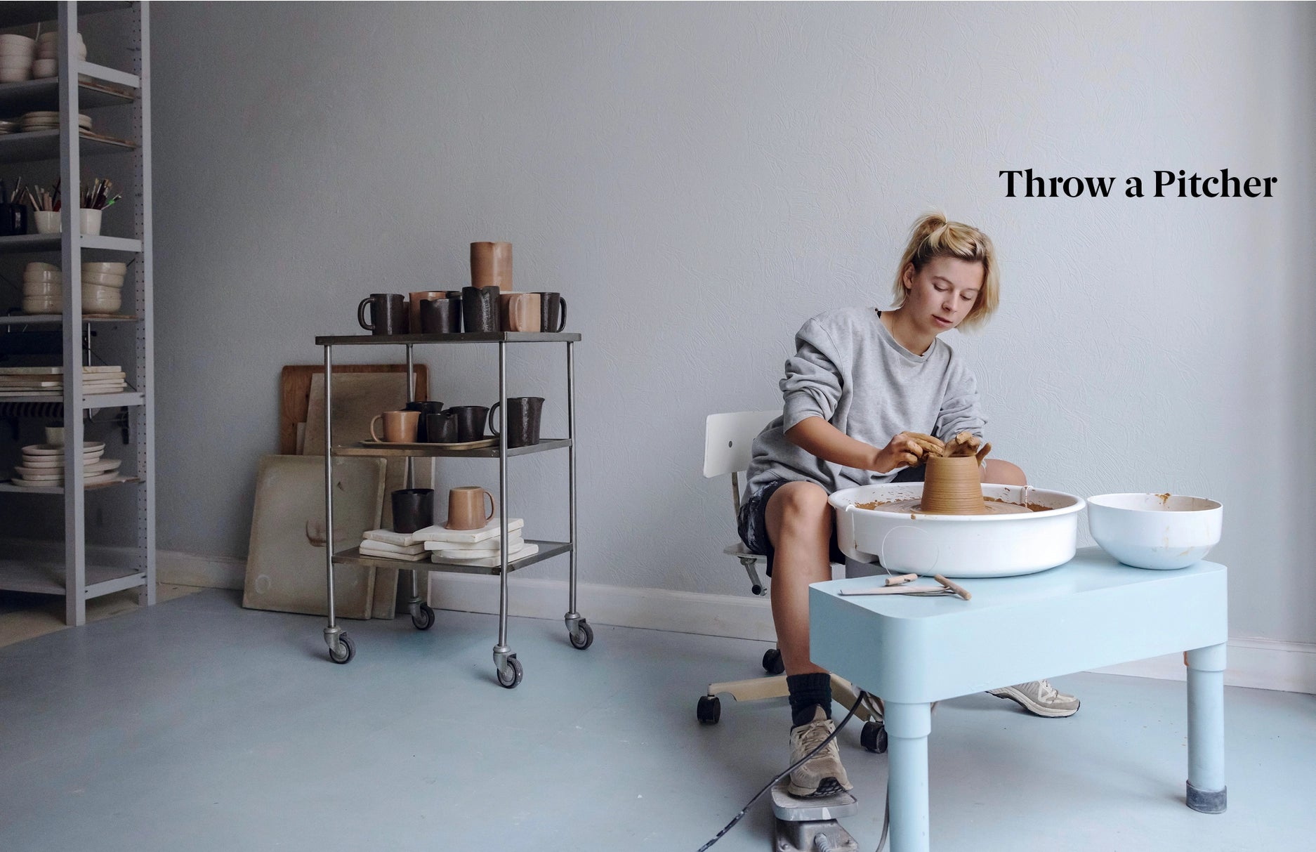 Person working with clay on a pottery wheel in a studio setting.
