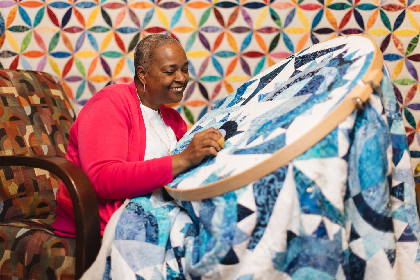 Woman holding a blue quilt in front of a colorful geometric-patterned wall.