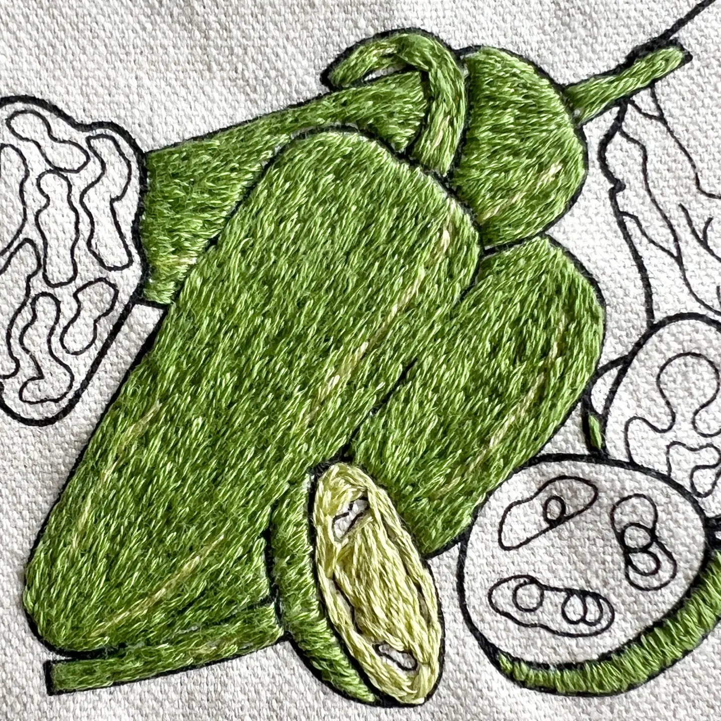 Embroidered green pepper design on a white fabric background
