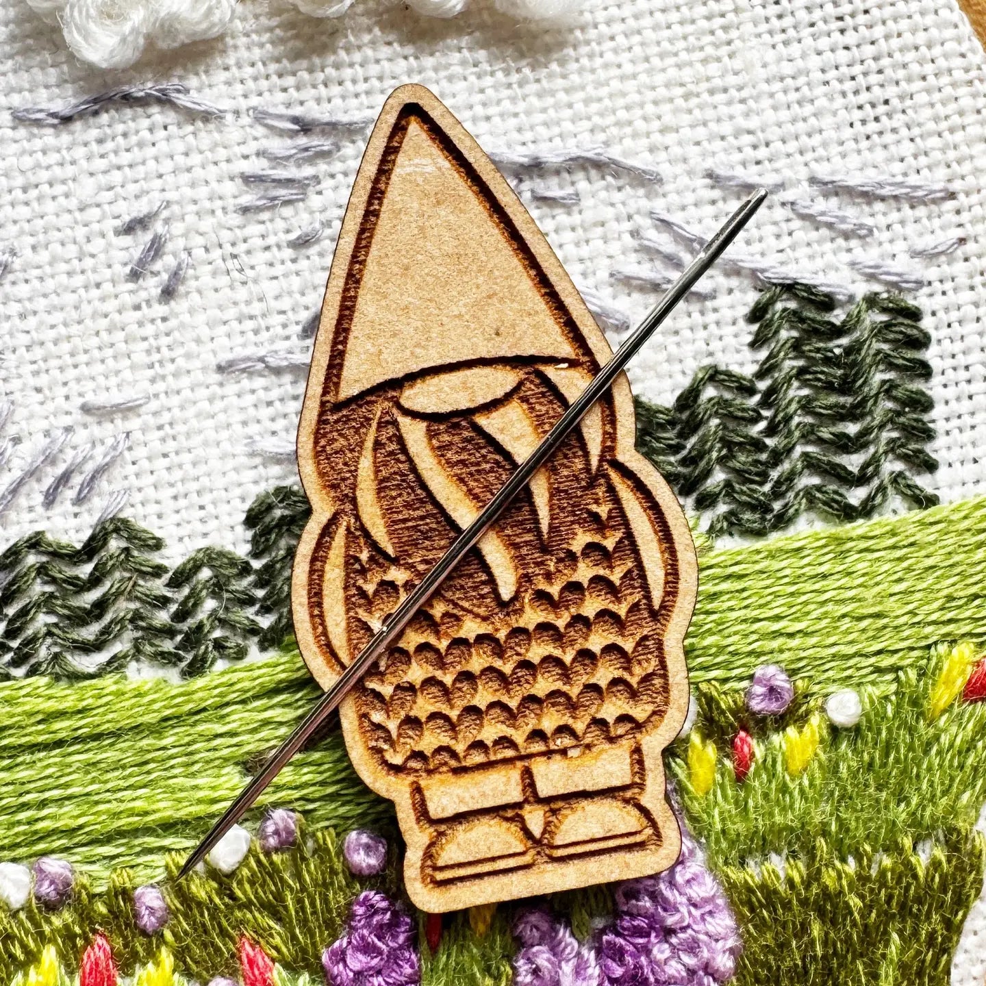 Wooden gnome needle minder on embroidered fabric with trees and flowers
