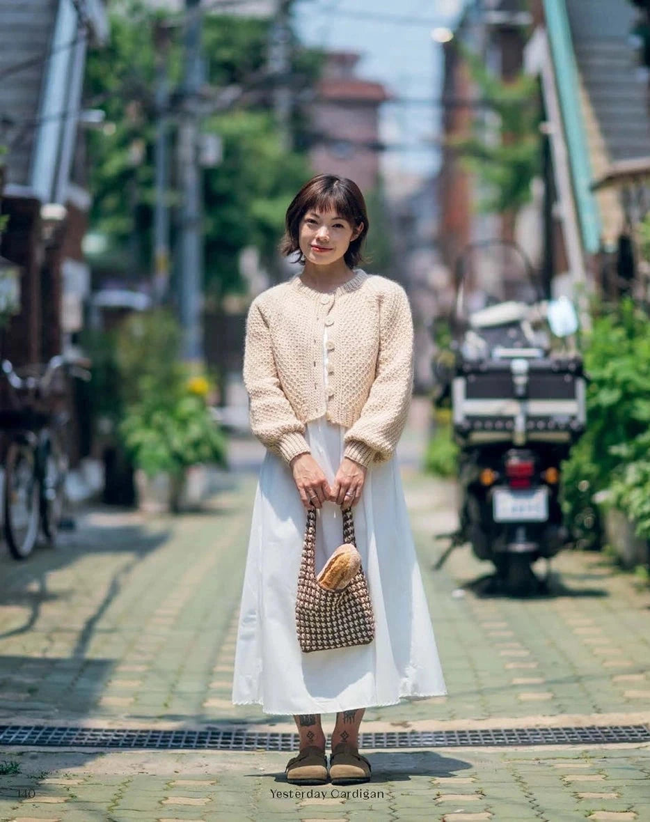 Woman in a beige cardigan and white skirt standing on a street 