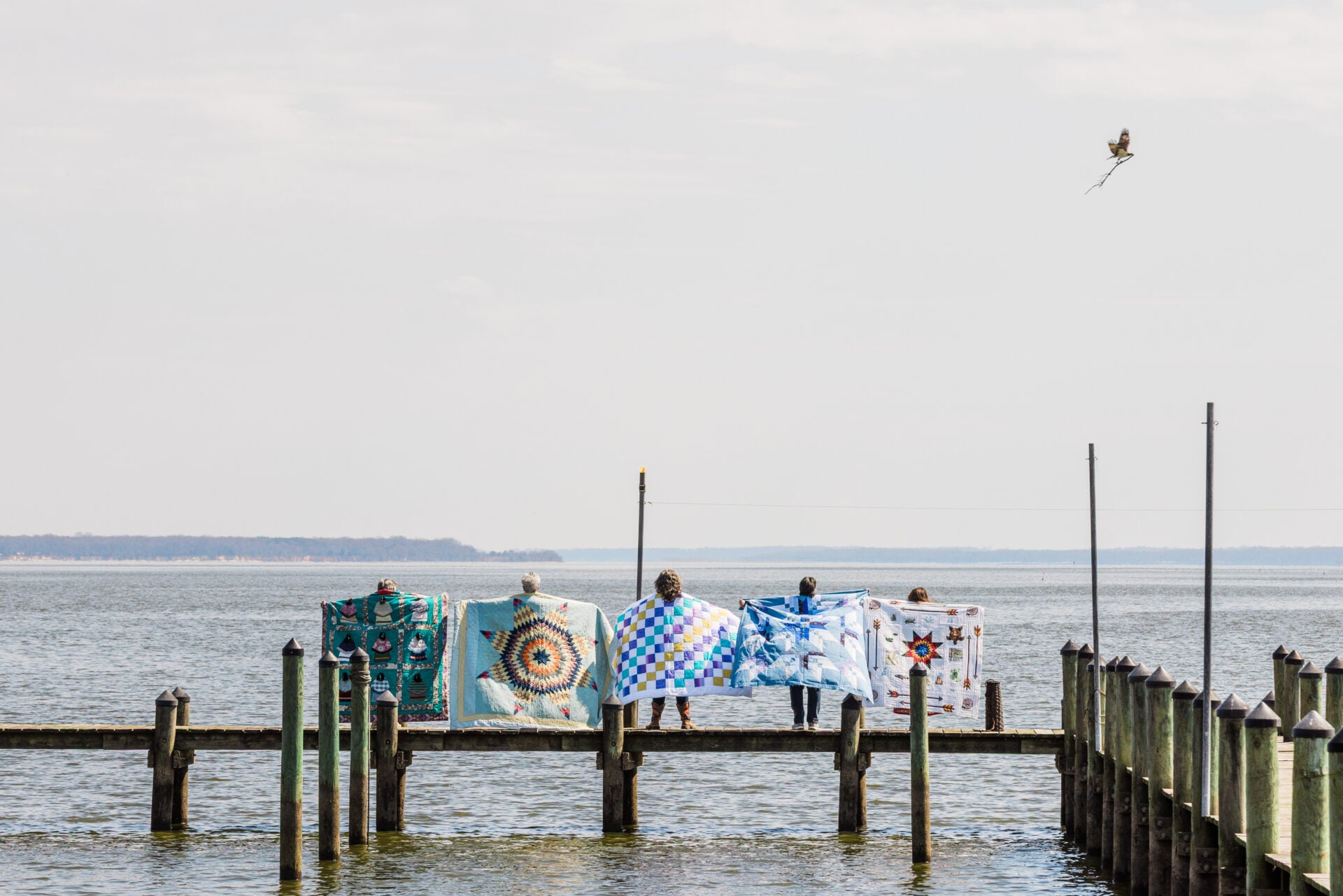 Quilts on a dock with a body of water and sky in the background