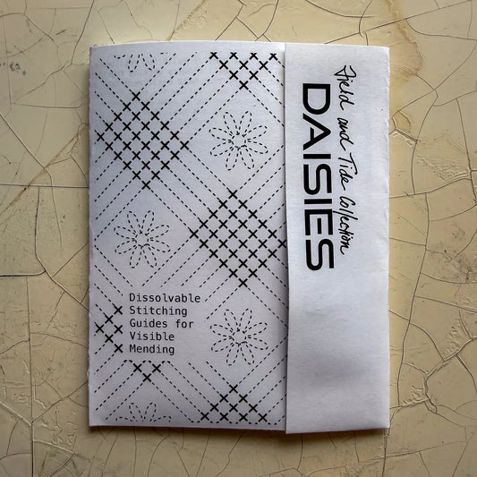 Folded paper with black stitching patterns and 'DAISIES' branding on a textured beige surface
